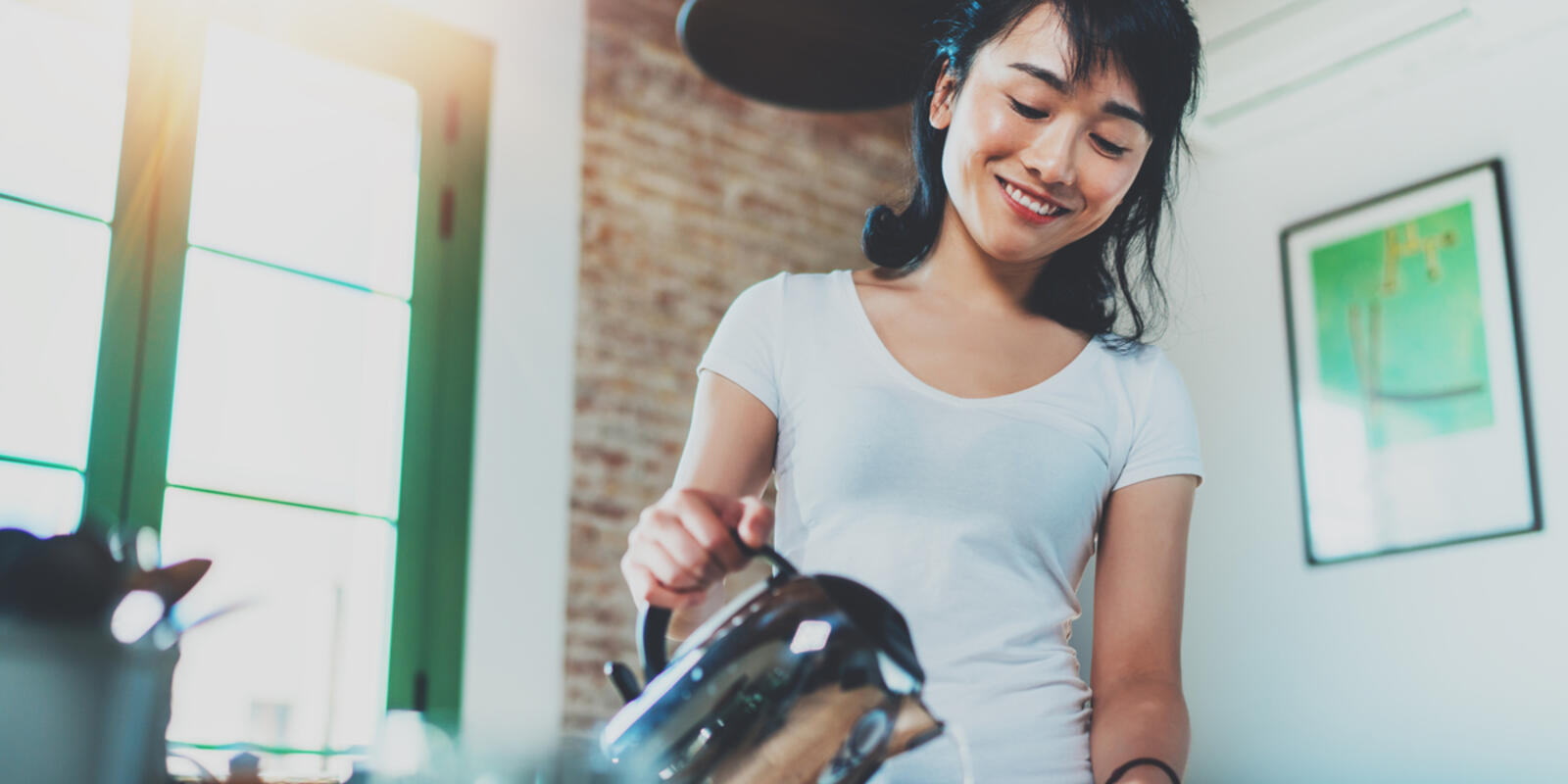 Smiling woman pouring water from electric kettle into cup