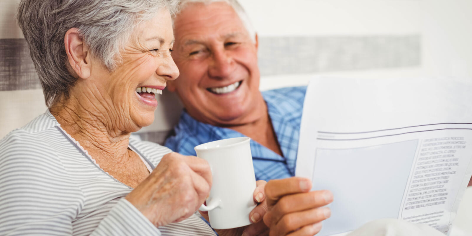 Older couple laughing, drinking coffee and reading newspaper