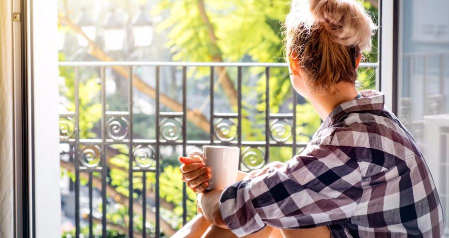 A young lady sits in the open balcony of her apartment with a cup of tea