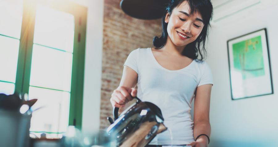 Smiling woman pouring water from electric kettle into cup