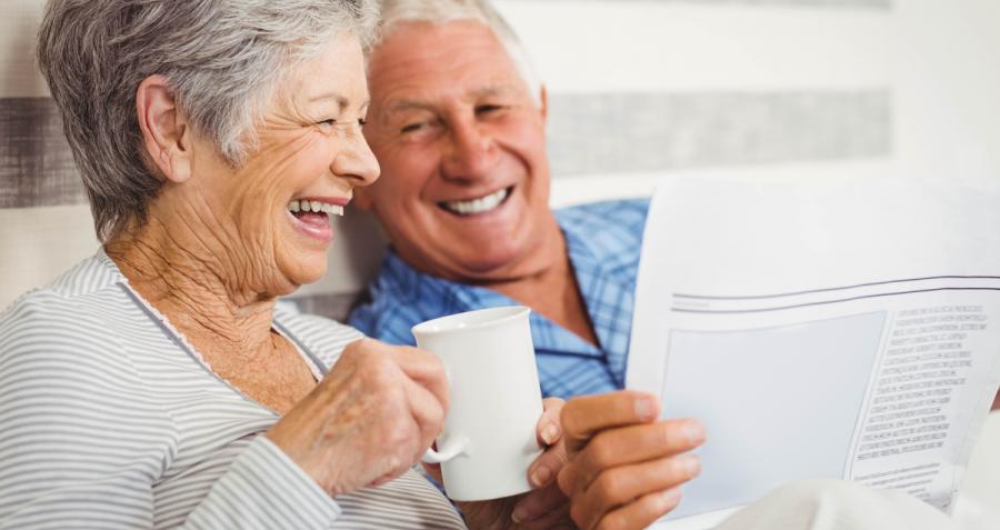 Older couple laughing, drinking coffee and reading newspaper